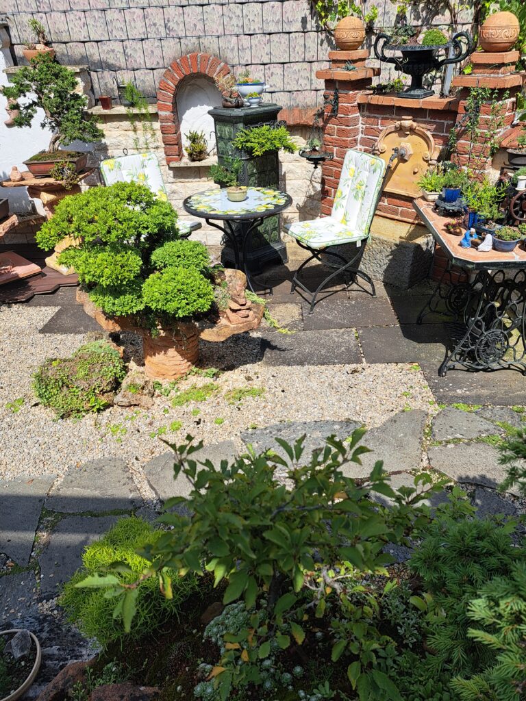 Runder Lavasteintisch mit Gartenstuhl zwischen Pflanzen und dekorativen Ziegelmauern