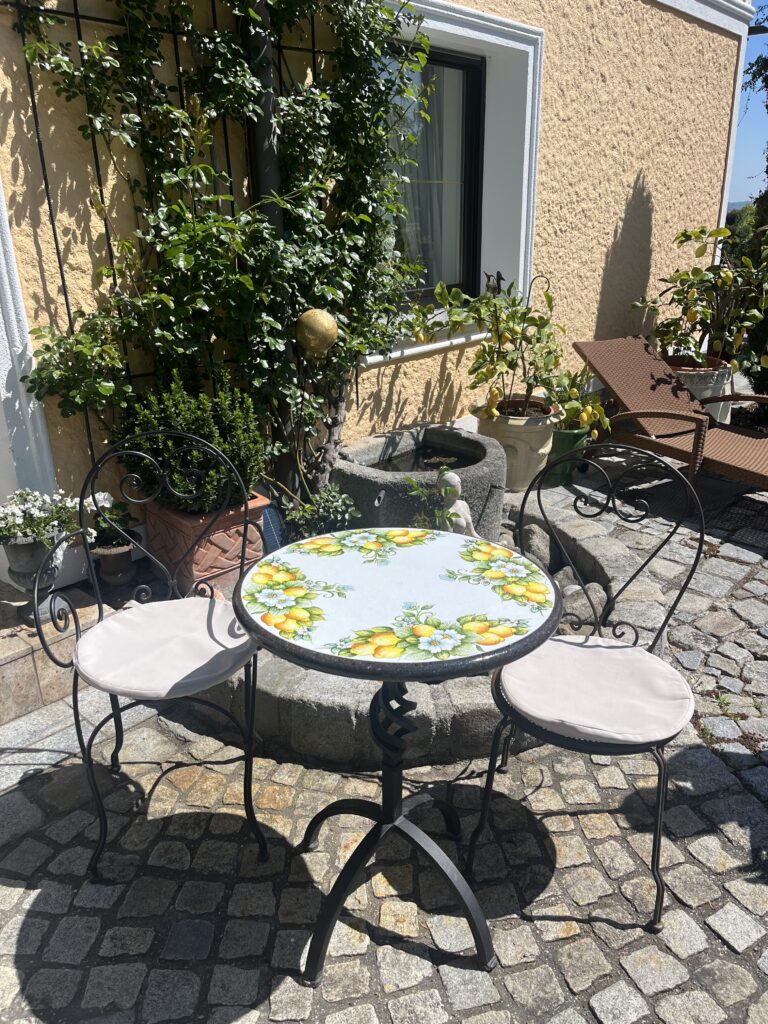 Runder Lavasteintisch mit Zitronendekor und vier Stühlen auf einer gepflasterten Terrasse